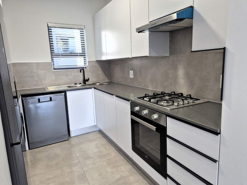 Modern kitchen featuring sleek white cabinetry, stone countertops, gas hob, built-in oven, extractor fan, and contemporary tiled finishes.