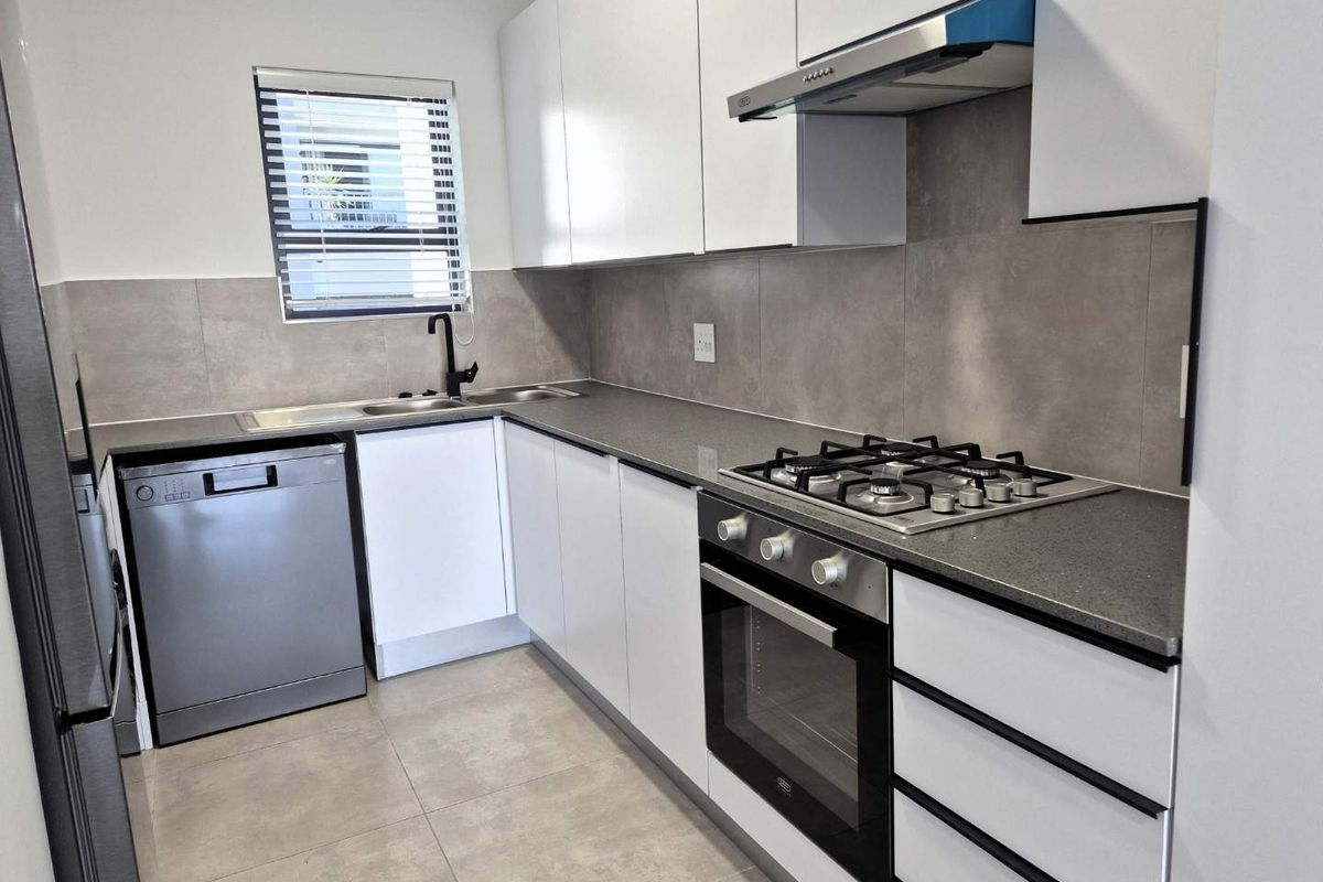Modern kitchen featuring sleek white cabinetry, stone countertops, gas hob, built-in oven, extractor fan, and contemporary tiled finishes.