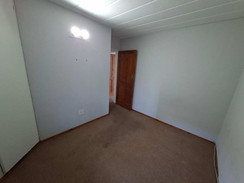 An empty bedroom featuring carpeted flooring, a built-in cupboard, and a wooden door, offering a blank canvas for potential updates.