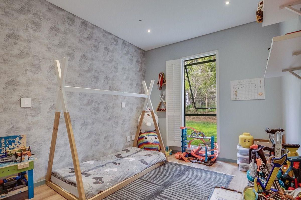 A bright bedroom featuring a textured accent wall, wood-look flooring, recessed ceiling lighting, and a large window with white plantation shutters.