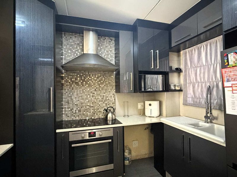 Modern kitchen featuring dark cabinetry, mosaic tile backsplash, stainless steel appliances, and stone countertops, with an efficient layout for cooking and preparation.