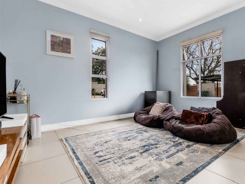 A bright living room featuring neutral tiled flooring, light blue walls, and large windows that provide ample natural light.