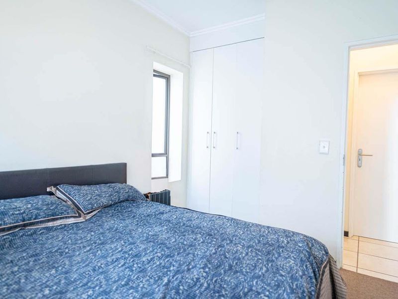 A bright bedroom featuring built-in cupboards, a combination of tiled and carpeted flooring, and a neutral interior finish.