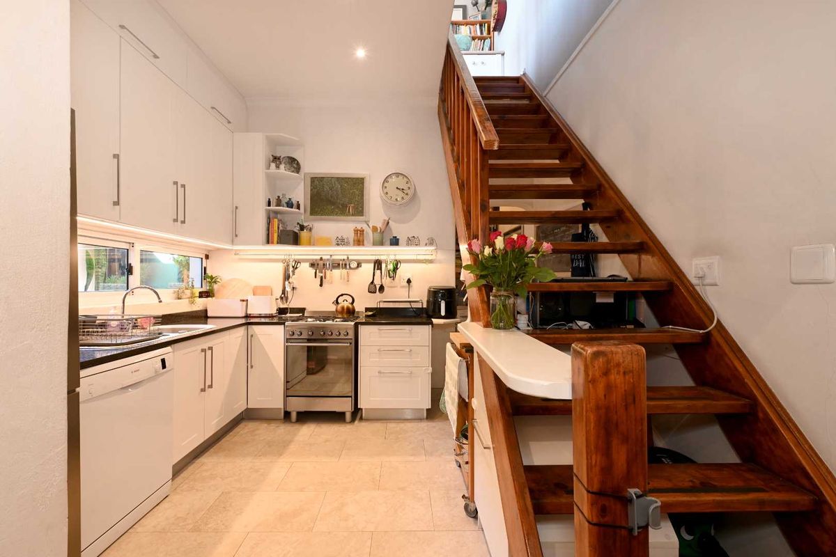 Compact kitchen featuring white cabinetry, stainless steel stove, under-cabinet lighting, and tiled flooring, adjacent to a wooden staircase.
