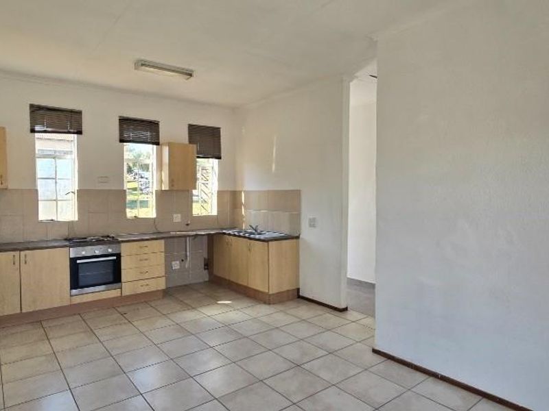 A functional, empty kitchen featuring light wood cabinetry, tiled flooring, a built-in oven, and a tiled backsplash with ample natural light.