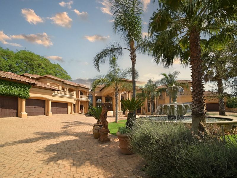 Grand front elevation of a luxury small holding featuring a paved driveway, multi-car garage, architectural columns, and a central water fountain.