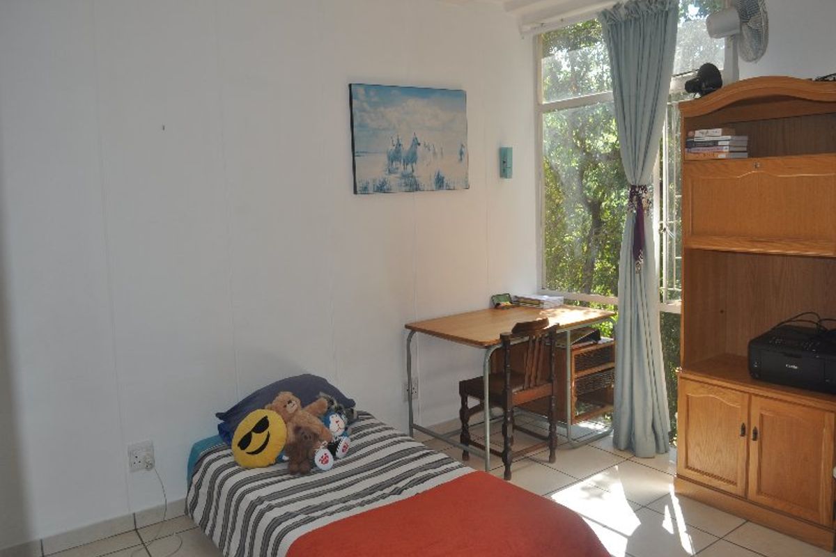 A functional bedroom featuring tiled flooring and a large window that provides natural light and garden views.
