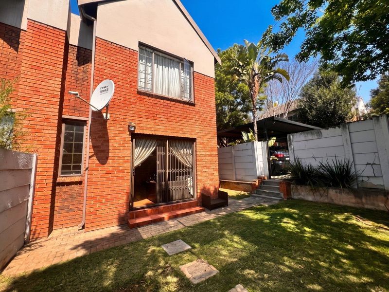 Rear view of a double-story brick townhouse featuring a small garden, paved walkway, sliding door access, and a private carport area.