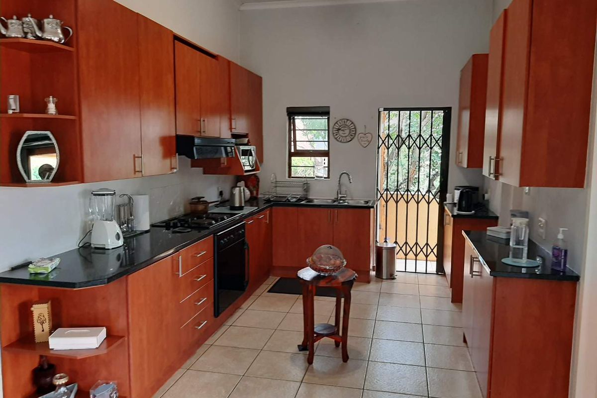 A functional kitchen featuring wooden cabinetry, dark granite countertops, a built-in oven, hob, extractor fan, and tiled flooring with direct access to the exterior.