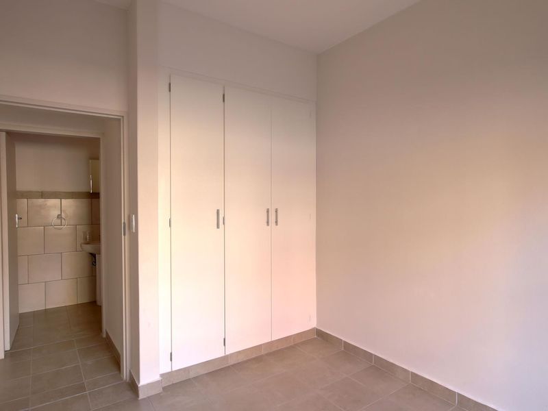 A clean, empty bedroom featuring neutral tiled flooring and white built-in cupboards, with an adjacent view into a tiled bathroom.