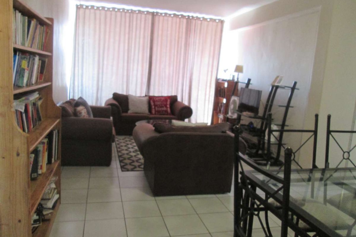 A living room area featuring tiled flooring and a large sliding glass door with curtains, providing access to the exterior.