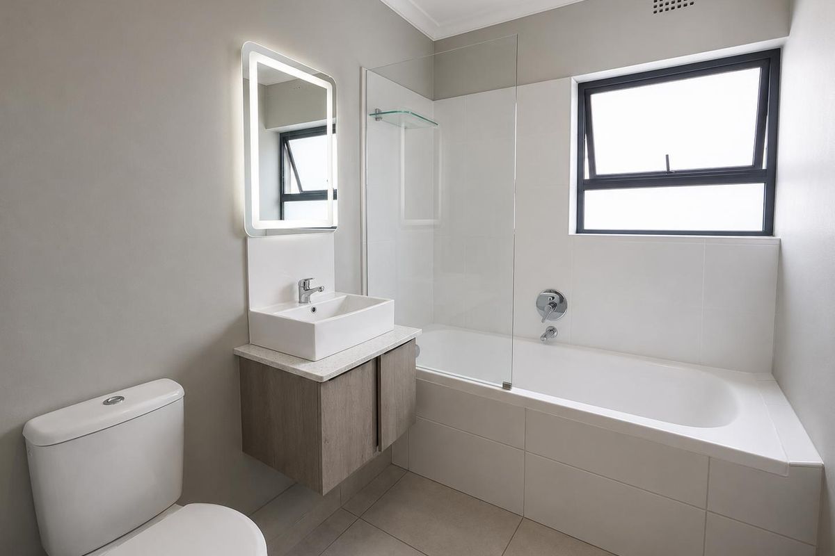 Modern bathroom featuring a floating vanity, vessel sink, illuminated mirror, and a bathtub with a glass shower screen and tiled surround.