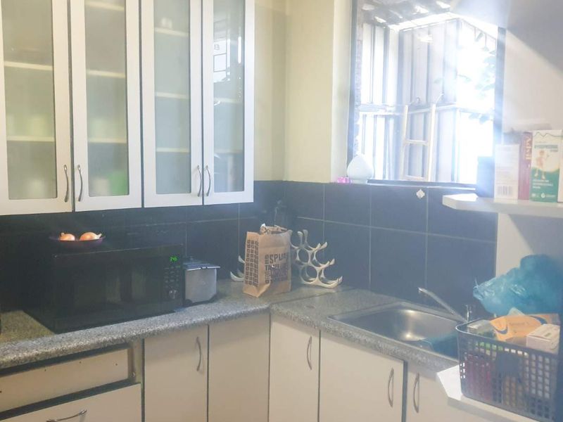 A functional kitchen area featuring built-in cabinetry, granite countertops, a stainless steel sink, and a tiled backsplash with glass-fronted upper storage units.