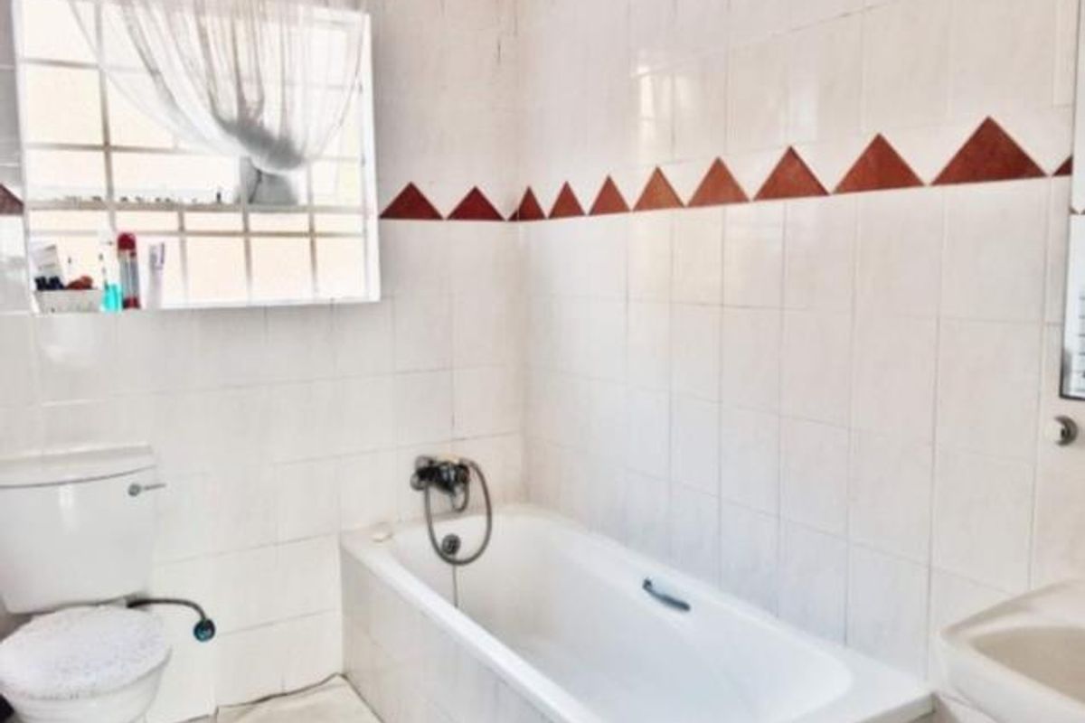 A functional bathroom featuring a standard bathtub, toilet, and wall-mounted basin with dated tiled finishes.