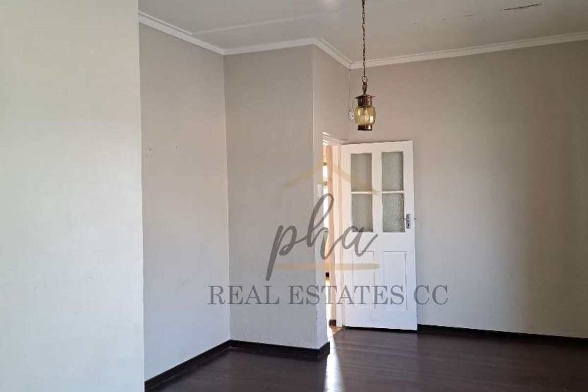 A spacious, empty living area featuring dark timber flooring, neutral wall tones, and a classic pendant light fixture.