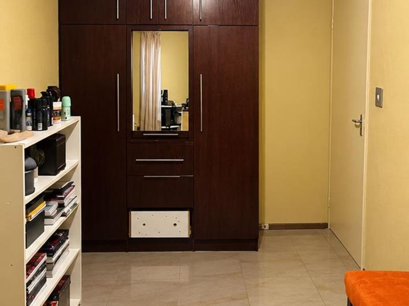 A bedroom featuring tiled flooring, a built-in dark wood wardrobe with a central mirror, and a ceiling-mounted light fixture.