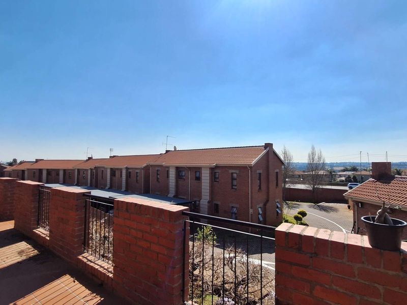 A spacious elevated balcony featuring a brick balustrade with metal railings and tiled flooring, overlooking the apartment complex grounds.