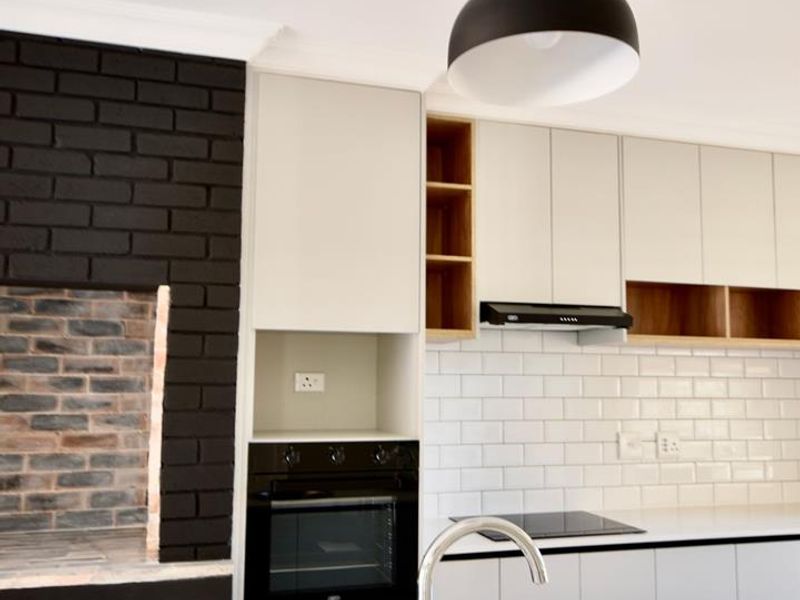 Modern kitchen featuring sleek white cabinetry, subway tile backsplash, built-in oven, electric hob, and a unique integrated brick fireplace feature.