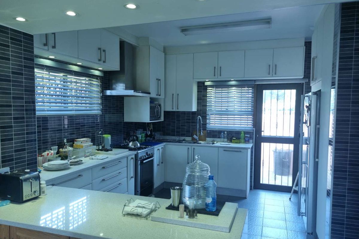 Modern kitchen featuring white cabinetry, dark tiled backsplash, stone countertops, stainless steel extractor fan, and integrated lighting with direct access to the exterior.