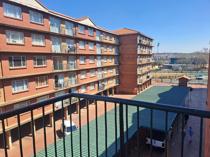 View of the apartment complex exterior featuring brick facade, multiple balconies, and a covered parking area within the residential grounds.