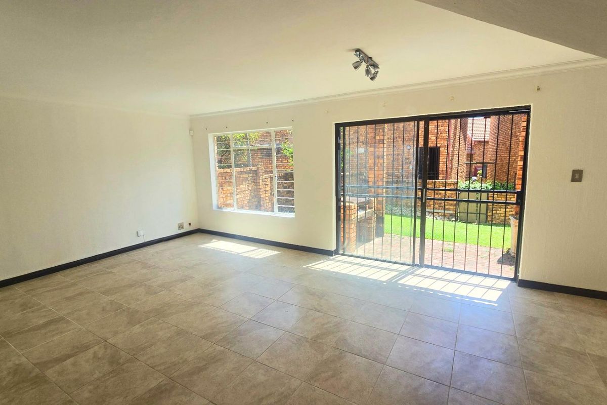 Spacious, empty living area featuring neutral tiled flooring, large windows, and a sliding glass door providing access to the rear garden.