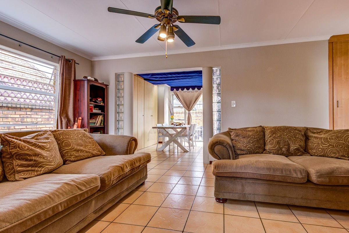 A living room featuring tiled flooring, a ceiling fan, and glass block accents leading into an adjacent dining area.