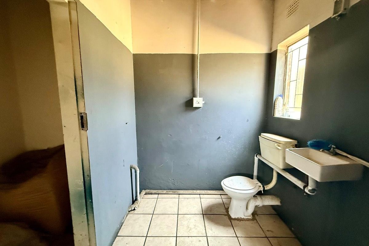 A basic bathroom featuring a standard toilet and wall-mounted basin with exposed plumbing and tiled flooring.