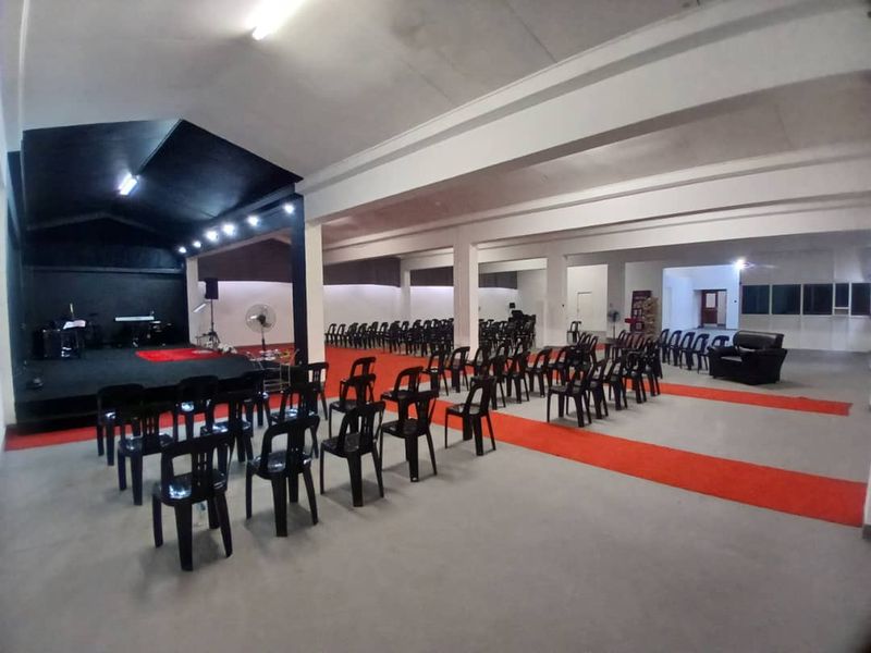 A large, open-plan event hall featuring a raised stage area, high ceilings with exposed beams, and durable concrete flooring, suitable for various business functions.