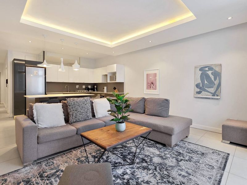 Modern open-plan living area featuring a contemporary kitchen with sleek cabinetry, a central island, and elegant recessed cove lighting throughout the space.