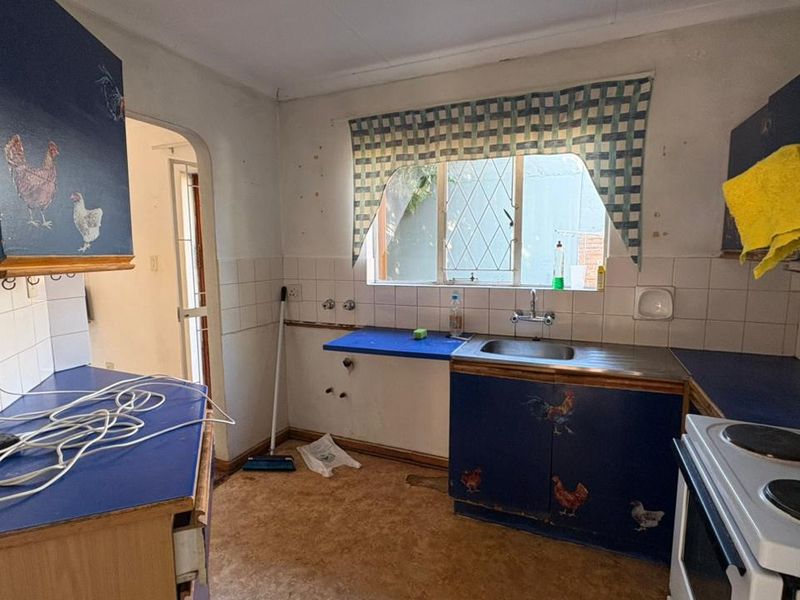 A dated kitchen featuring original cabinetry, a stainless steel sink, and tiled splashbacks, requiring modernization and cosmetic updates to improve functionality and aesthetic appeal.