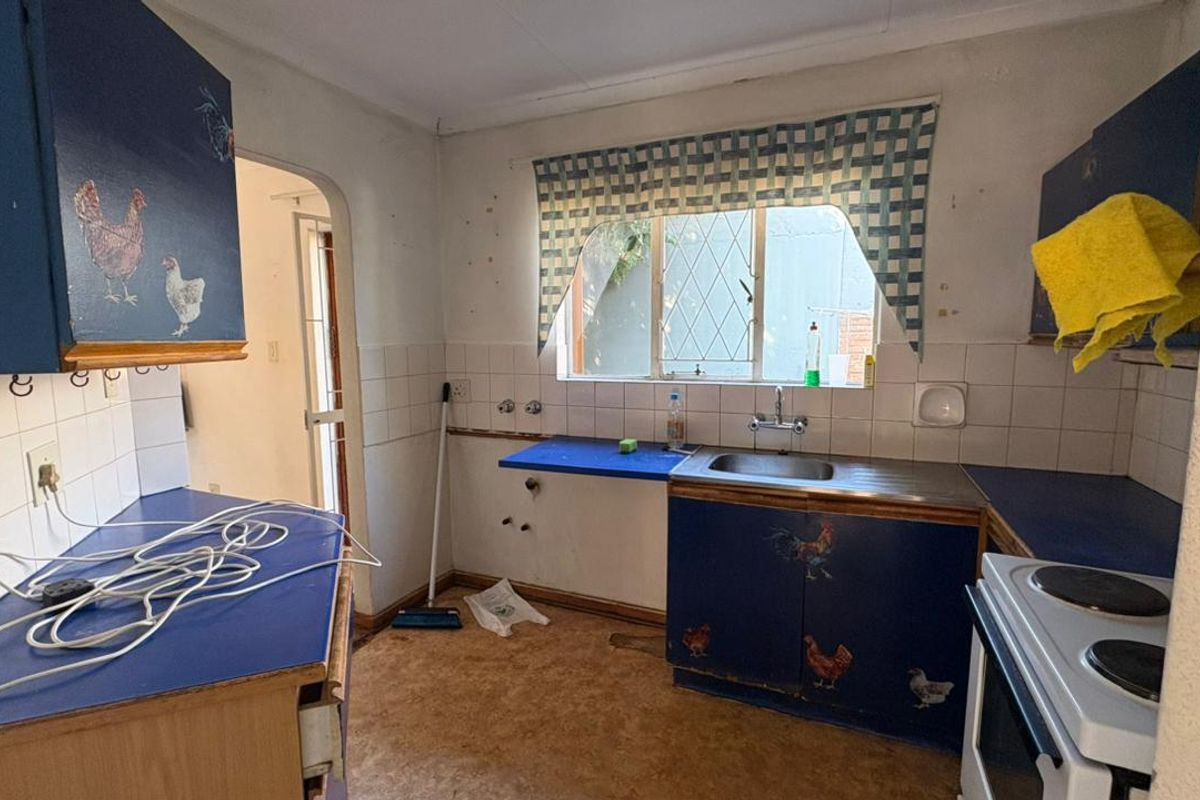 A dated kitchen featuring original cabinetry, a stainless steel sink, and tiled splashbacks, requiring modernization and cosmetic updates to improve functionality and aesthetic appeal.