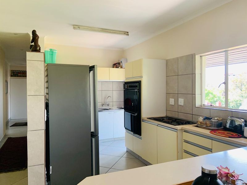 A functional kitchen featuring built-in cabinetry, a tiled backsplash, integrated oven and hob, and tiled flooring with a view through the window.
