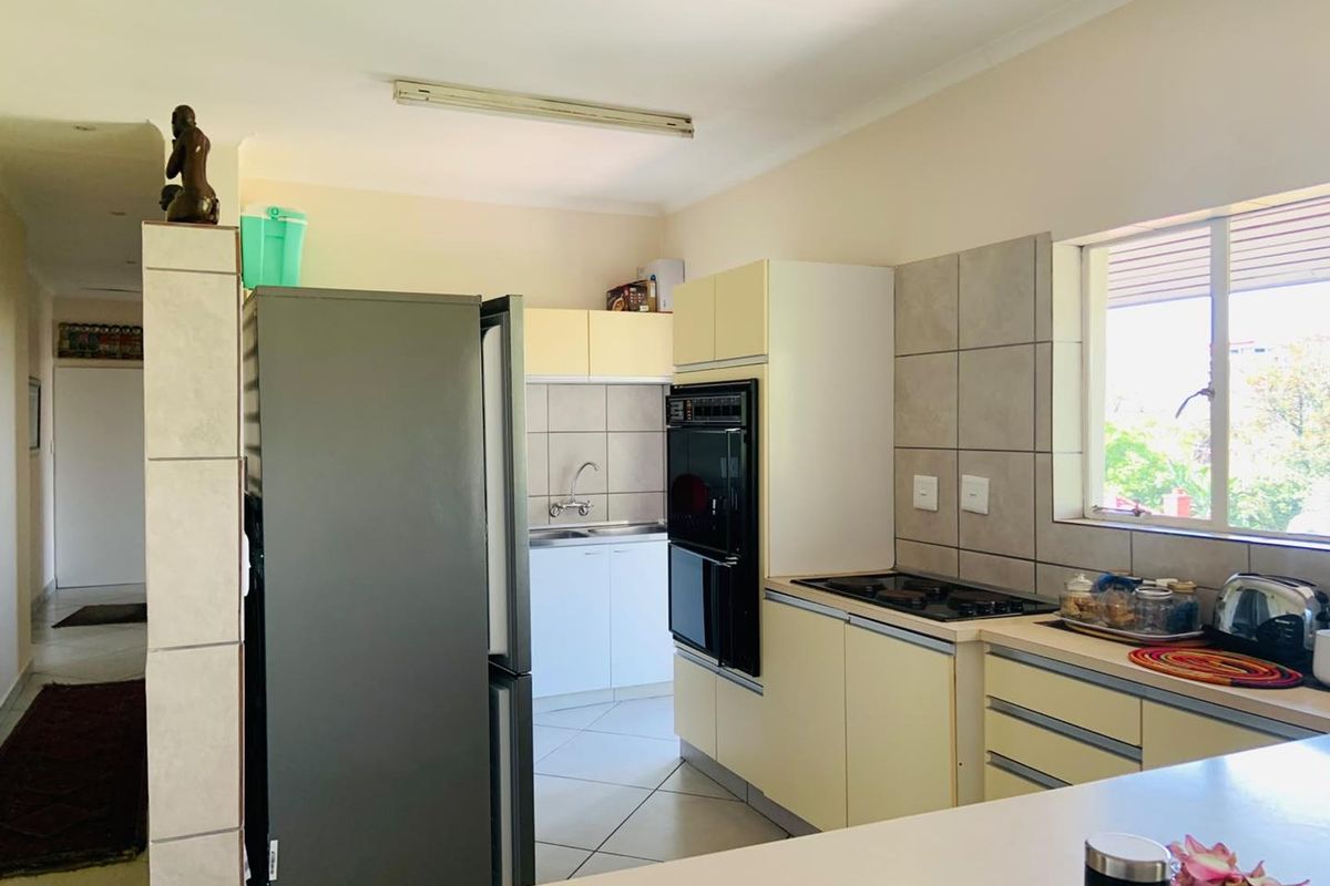 A functional kitchen featuring built-in cabinetry, a tiled backsplash, integrated oven and hob, and tiled flooring with a view through the window.