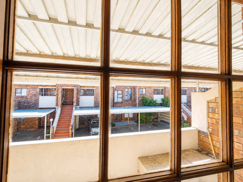 View from an interior window looking out over a townhouse complex courtyard with brick facades, carports, and communal staircases.