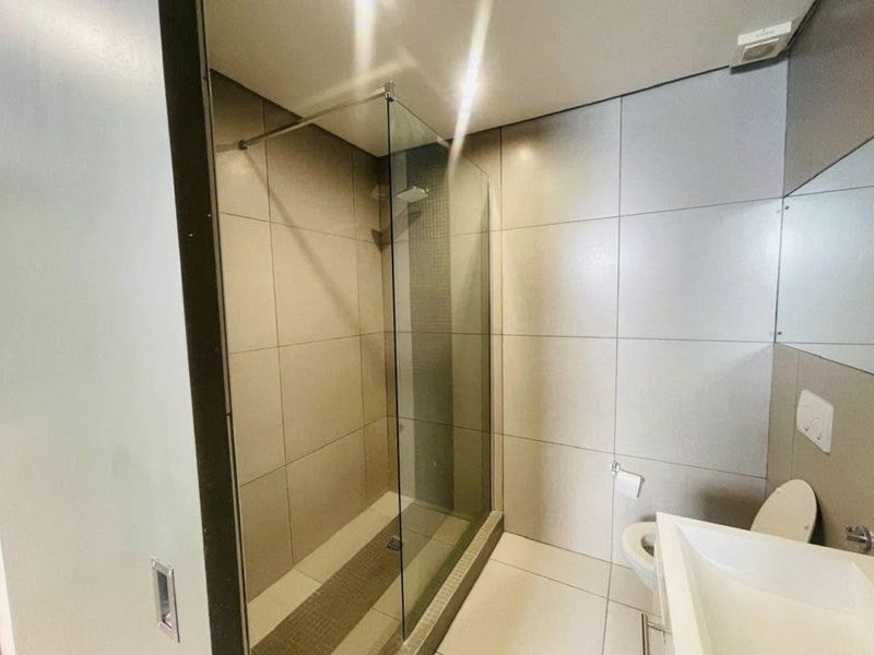 Modern bathroom featuring a spacious walk-in shower with glass screen, wall-mounted toilet, and contemporary vanity basin with neutral floor-to-ceiling tiling.