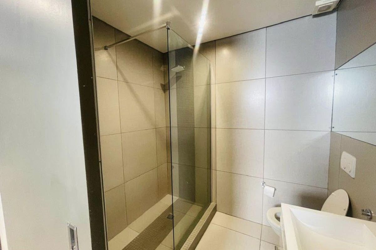 Modern bathroom featuring a spacious walk-in shower with glass screen, wall-mounted toilet, and contemporary vanity basin with neutral floor-to-ceiling tiling.