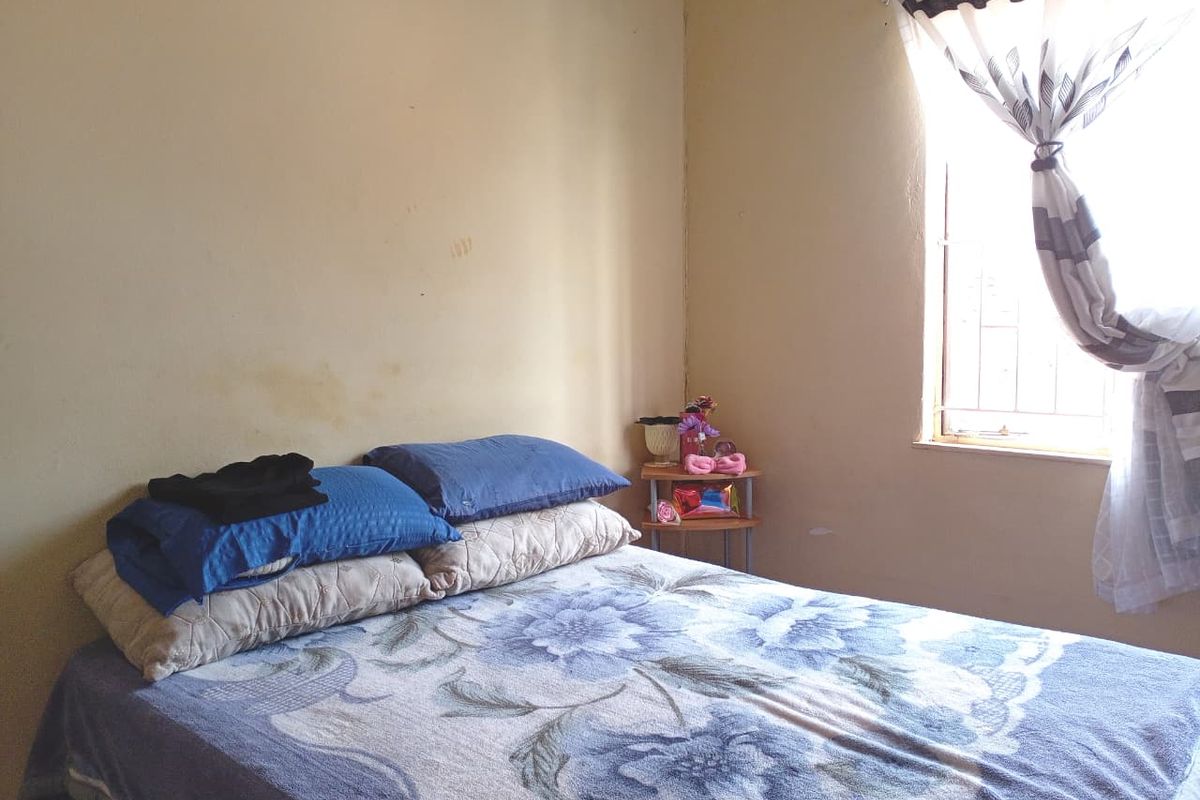 A bedroom featuring a window with security bars and plain wall finishes, providing a functional sleeping space.