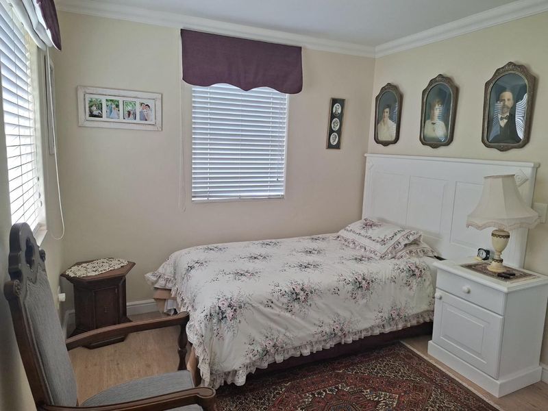A well-maintained bedroom featuring laminate flooring, crown molding, and a built-in headboard, illuminated by natural light through venetian blinds.