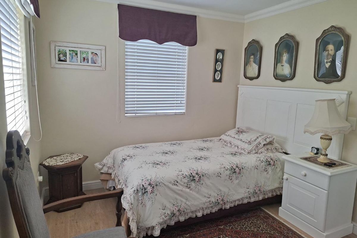 A well-maintained bedroom featuring laminate flooring, crown molding, and a built-in headboard, illuminated by natural light through venetian blinds.
