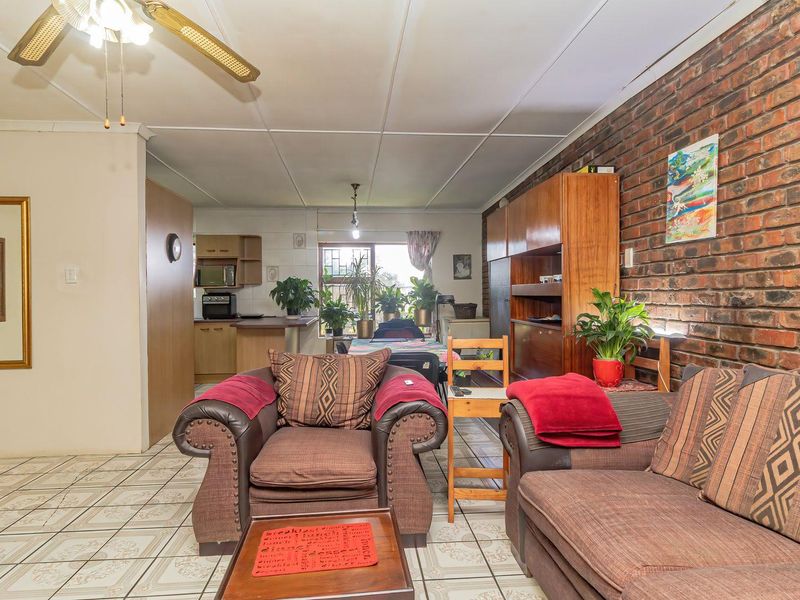 Open-plan living and kitchen area featuring an exposed brick feature wall, tiled flooring, and a functional kitchen layout with a breakfast counter.