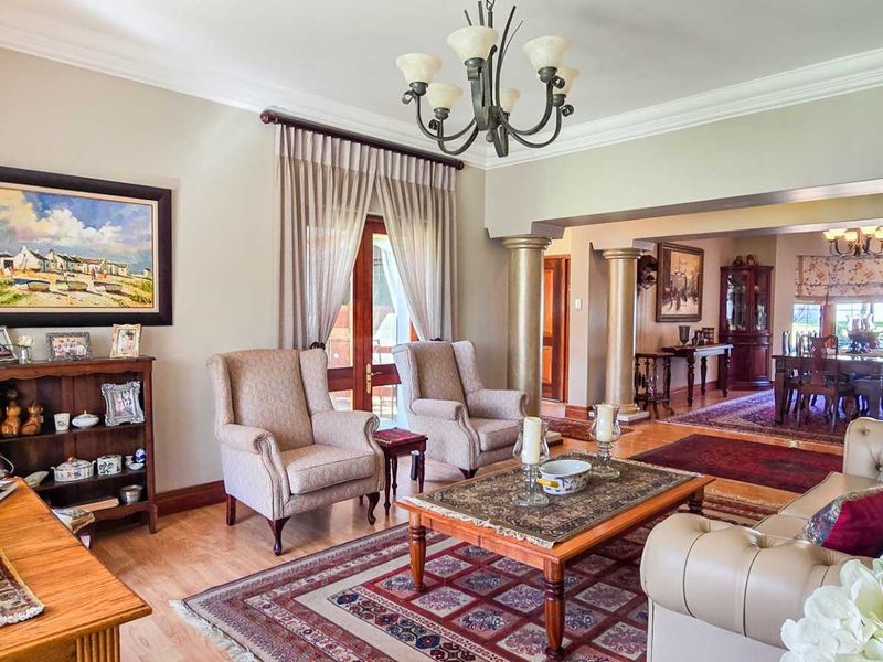 Spacious open-plan living and dining area featuring decorative columns, crown molding, hardwood flooring, and elegant chandelier lighting with access to outdoor space.