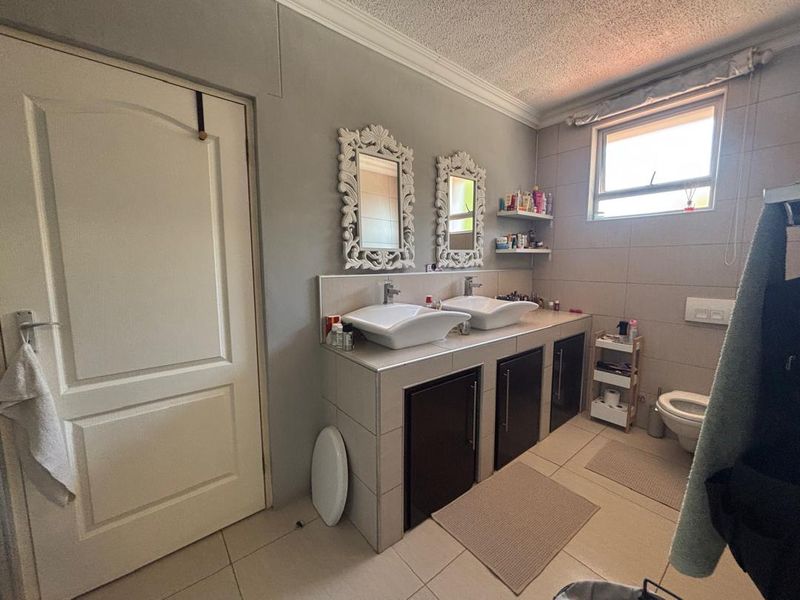 Bathroom featuring a double vanity with vessel sinks, tiled surfaces, and a wall-mounted toilet.