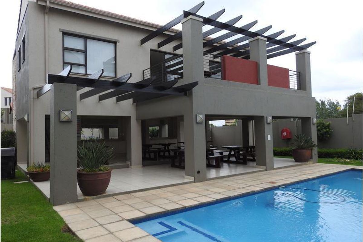 Rear view of the property featuring a covered patio area, a swimming pool with paved surround, and an upper-level balcony with pergola structure.