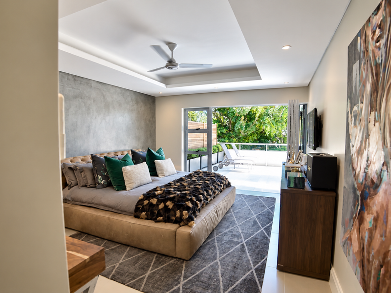 Spacious modern bedroom featuring a tray ceiling, recessed lighting, a feature wall, and large sliding glass doors opening onto a private balcony.