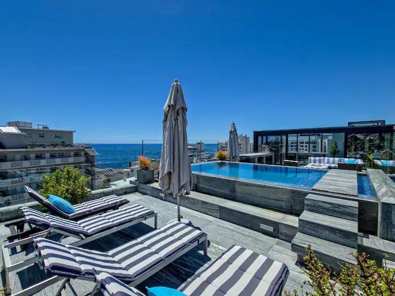 A luxury penthouse rooftop terrace featuring a modern swimming pool, stone decking, and glass balustrades with panoramic ocean views.