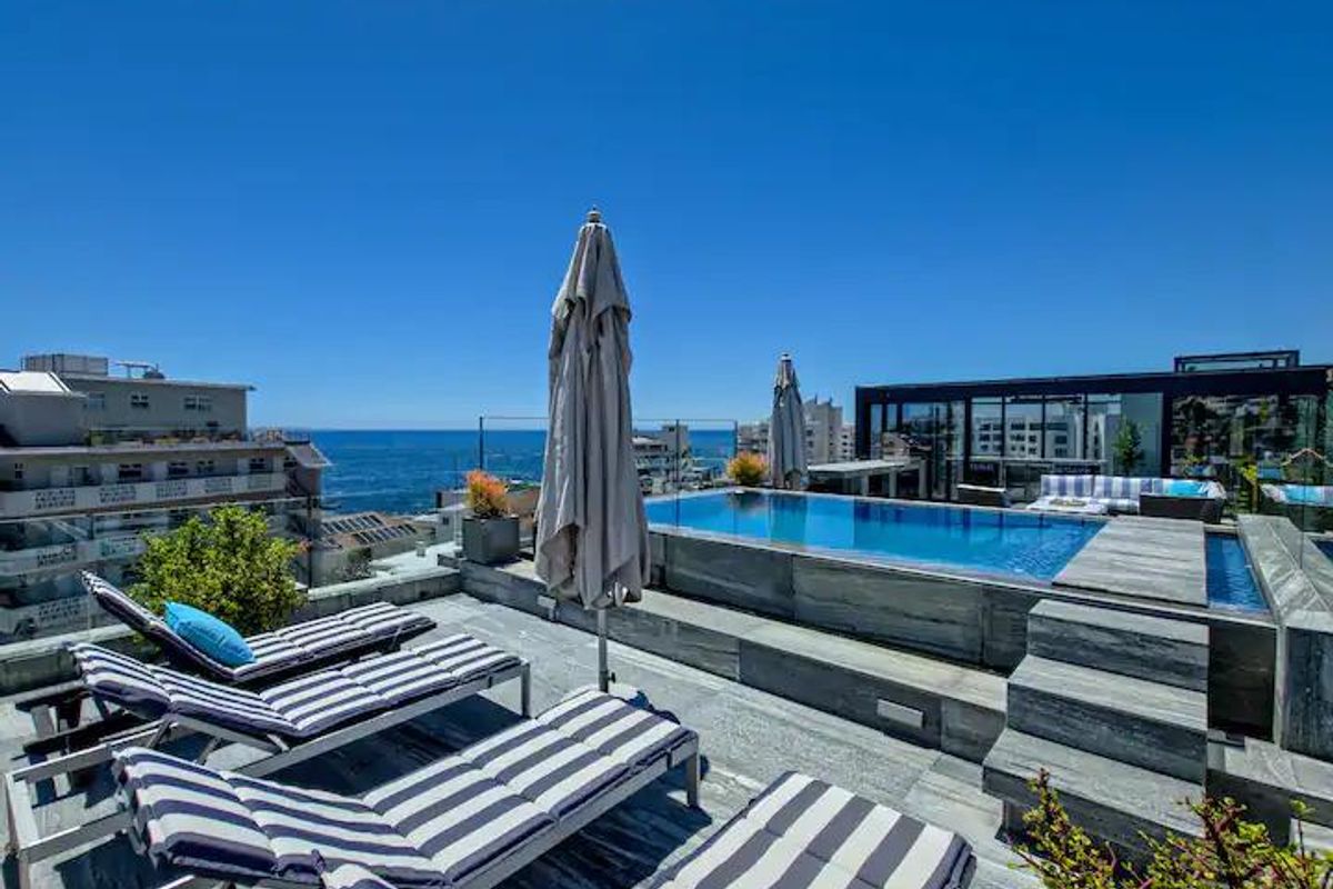 A luxury penthouse rooftop terrace featuring a modern swimming pool, stone decking, and glass balustrades with panoramic ocean views.