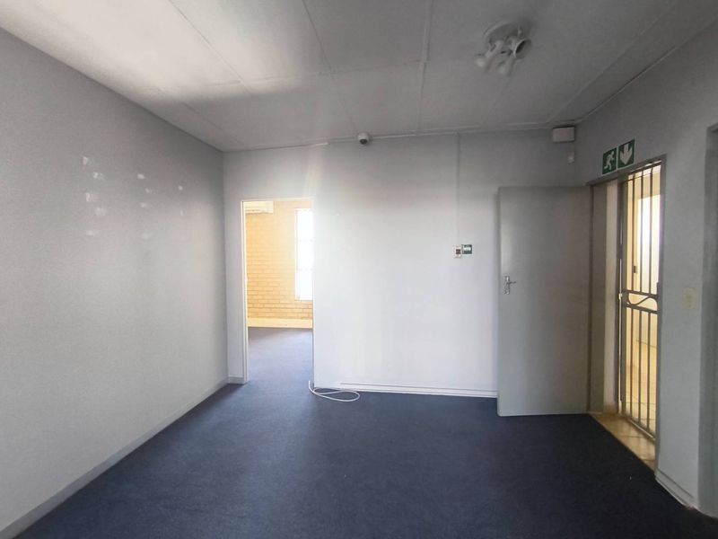 An empty office space featuring carpeted flooring, a security gate, and basic lighting, suitable for a professional workspace setup.