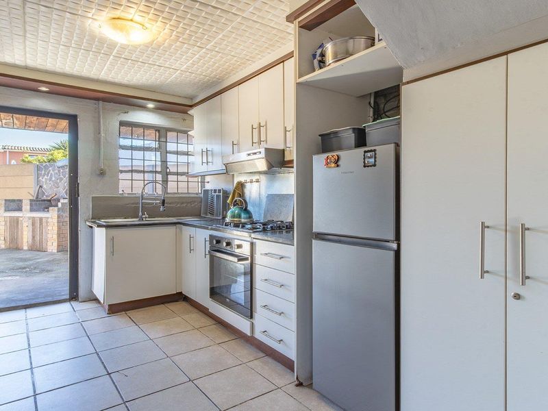 A functional kitchen featuring built-in cabinetry, a gas hob, oven, and tiled flooring, with direct access to an outdoor patio area.
