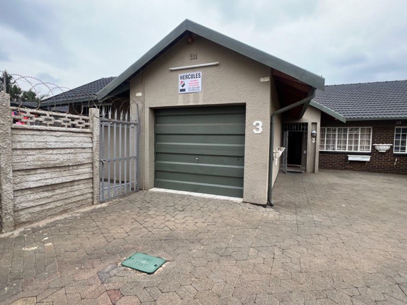 Front exterior view of the property featuring a single garage, paved driveway, and secure perimeter fencing with razor wire.