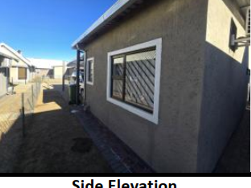 Side elevation of the house featuring textured exterior walls, aluminium window frames with security bars, and a paved walkway along the perimeter.